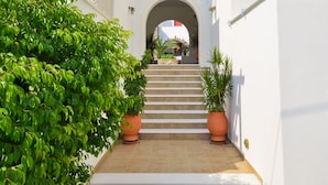 A white building with a central archway, a staircase leading to an upper level, and potted plants along the pathway. - Anthi Studios (Naxos)