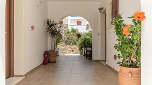 A hallway with a tiled floor, a potted plant, and a view of a courtyard with a stone wall and greenery. - Anthi Studios (Naxos)