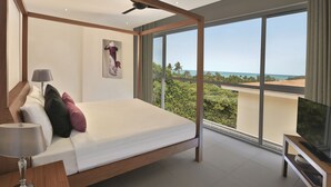 Een moderne slaapkamer met een groot bed, een plafondventilator, een televisie en een balkon met uitzicht op de oceaan.