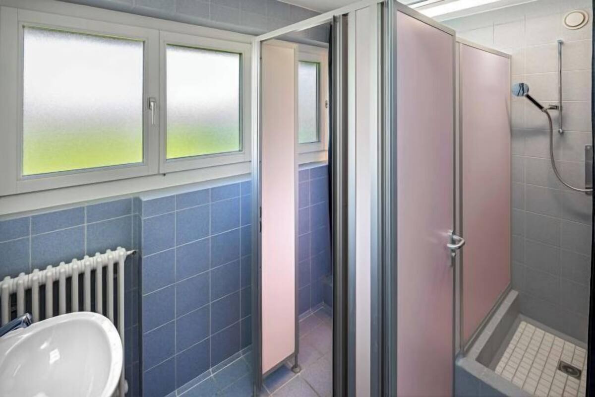 A bathroom with a white sink, blue tiles, a shower with a glass door, and a radiator.