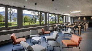 A spacious indoor area with multiple seating arrangements and large windows offering a view of a park and distant buildings. - Youth Hostel Rapperswil-Jona (Rapperswil-Jona)