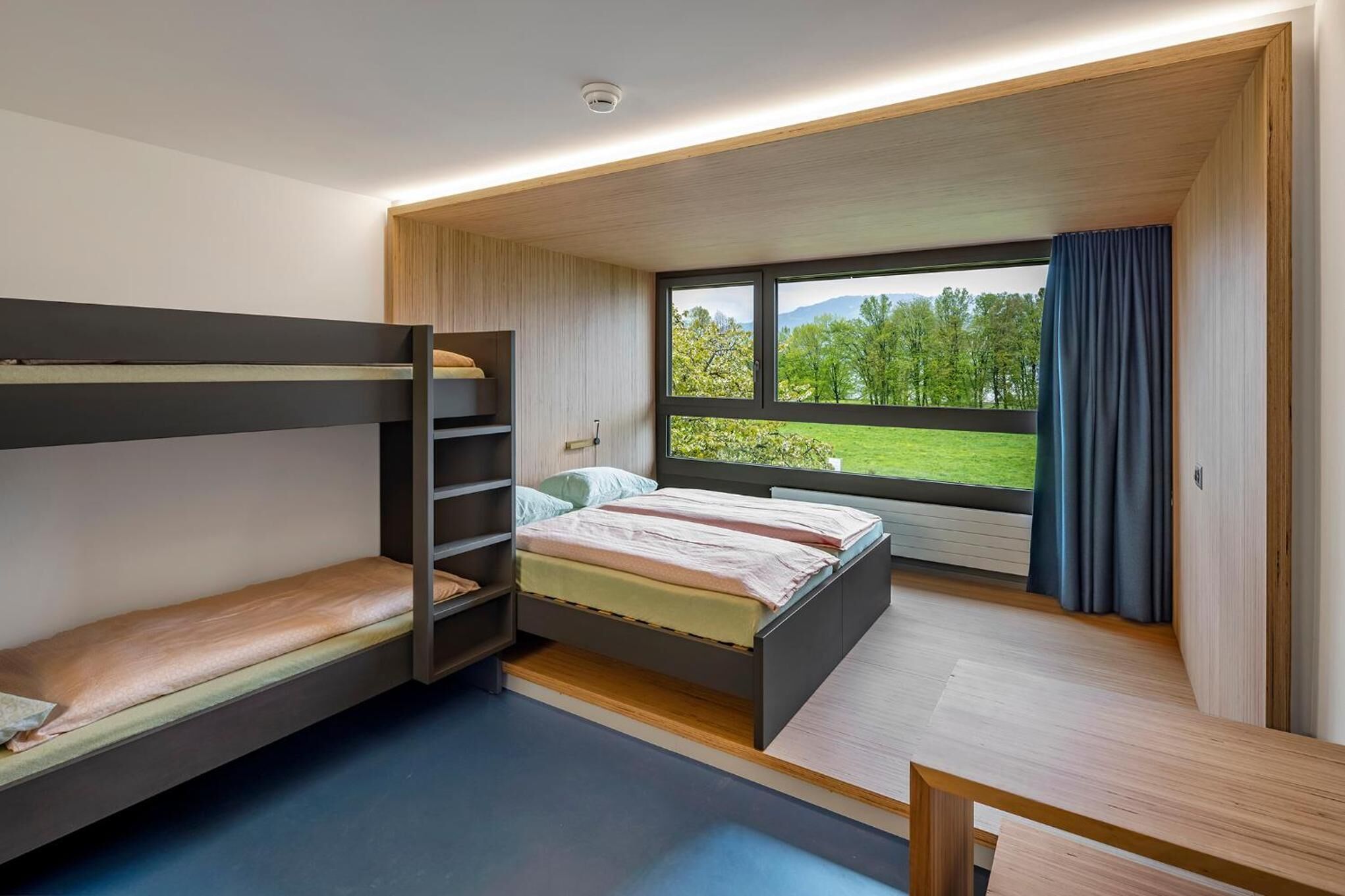 Une chambre moderne avec des lits superposés, une grande fenêtre donnant sur un paysage verdoyant et des étagères intégrées.
