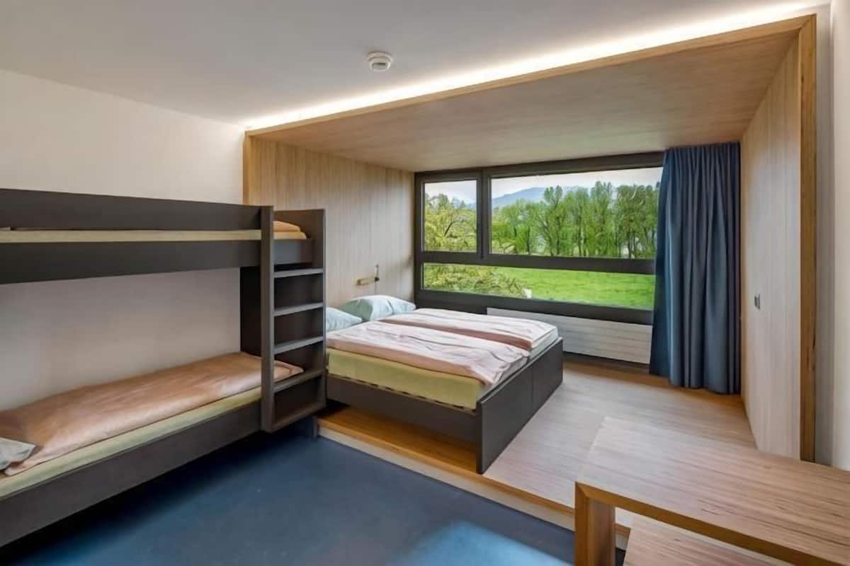 A bunk bed room with a window view, a desk, and a small table.