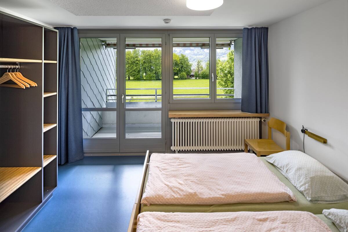 A bedroom with two beds, a radiator, a wooden desk, and a wardrobe.
