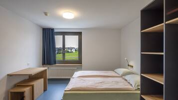 Un dormitorio con cama, escritorio y ventana con vistas a casas.