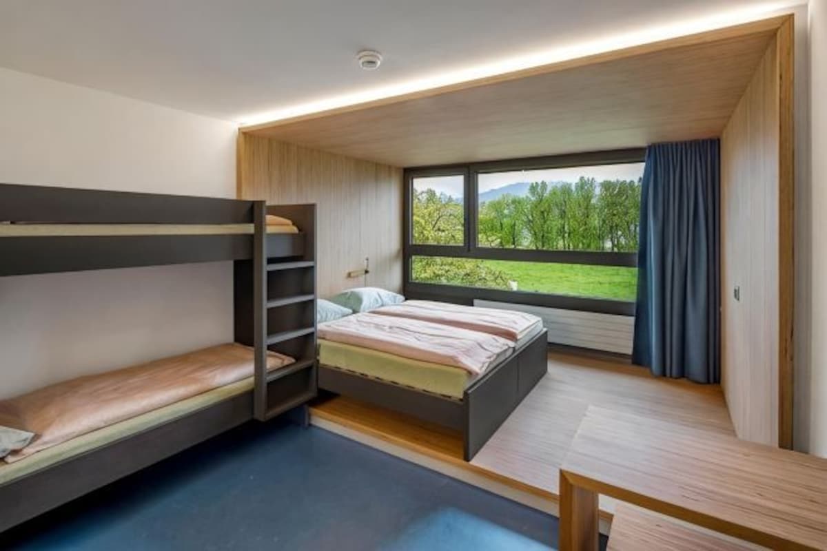 A bunk bed room with a window view, a desk, and a small table.