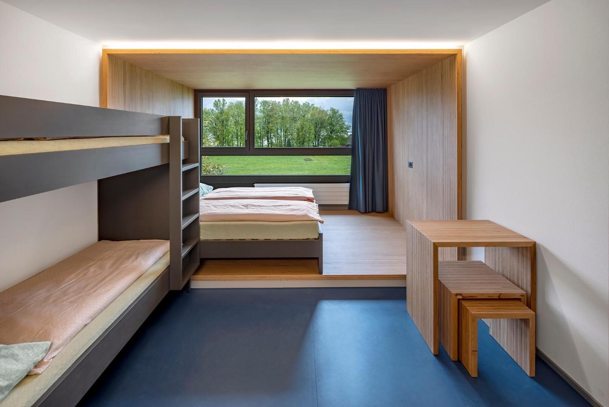 Ein kleines Schlafzimmer mit Etagenbetten, einem kleinen Schreibtisch und einem Fenster mit Blick auf Grünflächen.