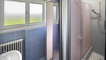 Une salle de bain avec un lavabo blanc, des murs recouverts de carreaux bleus, des fenêtres à vitres dépolies et un espace douche.