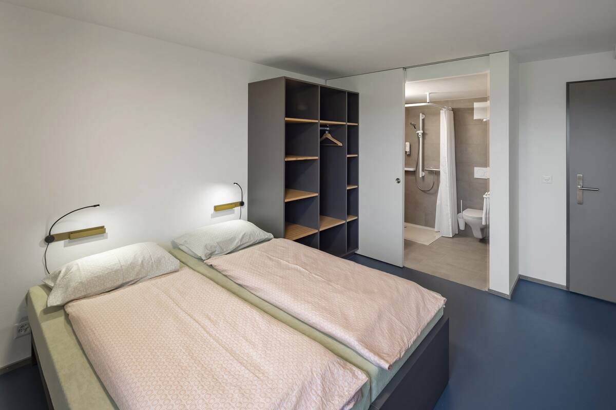 A bedroom with two beds, a wardrobe, and a bathroom visible through an open door.