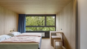 A bedroom with two beds, a window with a view of trees, a desk, and a chair. - Youth Hostel Rapperswil-Jona (Rapperswil-Jona)