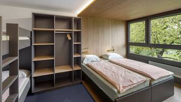A modern bedroom with a built-in wardrobe, a large window with a view of trees, and a bed with a wooden headboard.