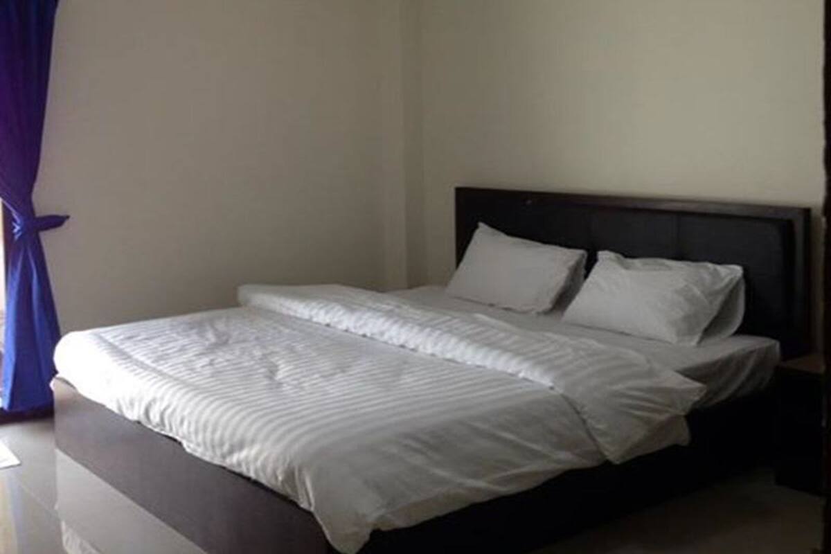 Una cama bien hecha con sábanas blancas y un cabecero oscuro en una habitación sencilla con paredes lisas.