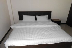 A neatly made bed with a dark headboard and white bedding in a simple room with a small wooden nightstand beside it.