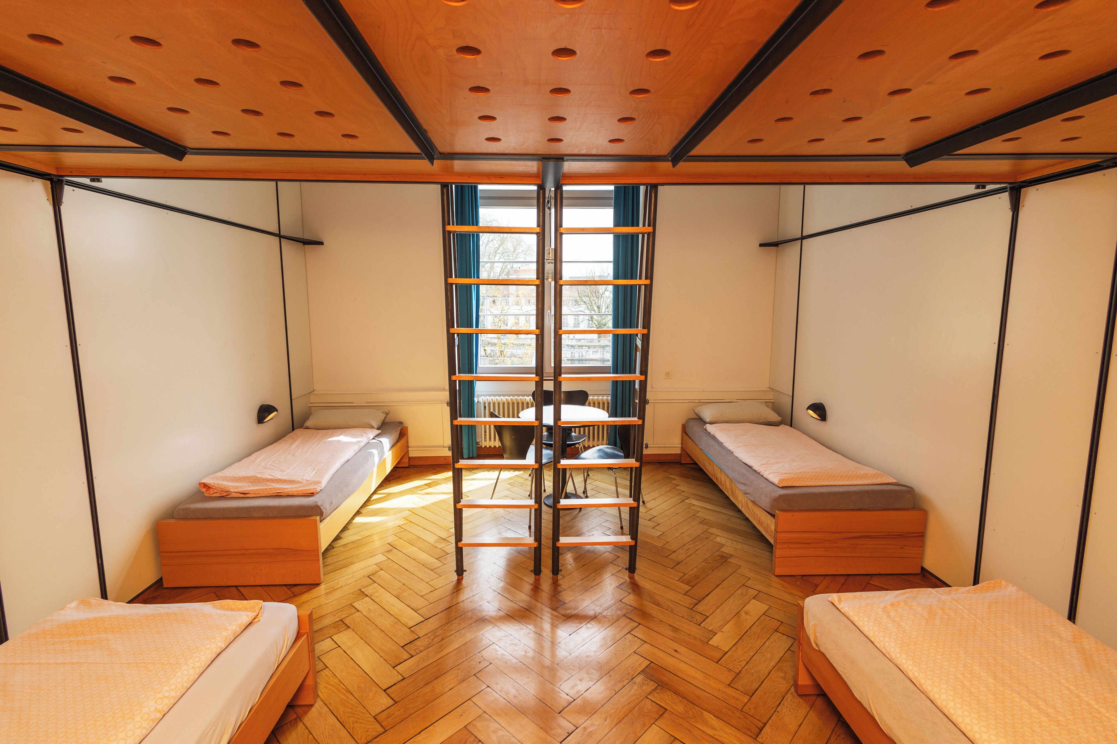 Una habitación con dos camas individuales, una mesa en el centro y una ventana con cortinas.
