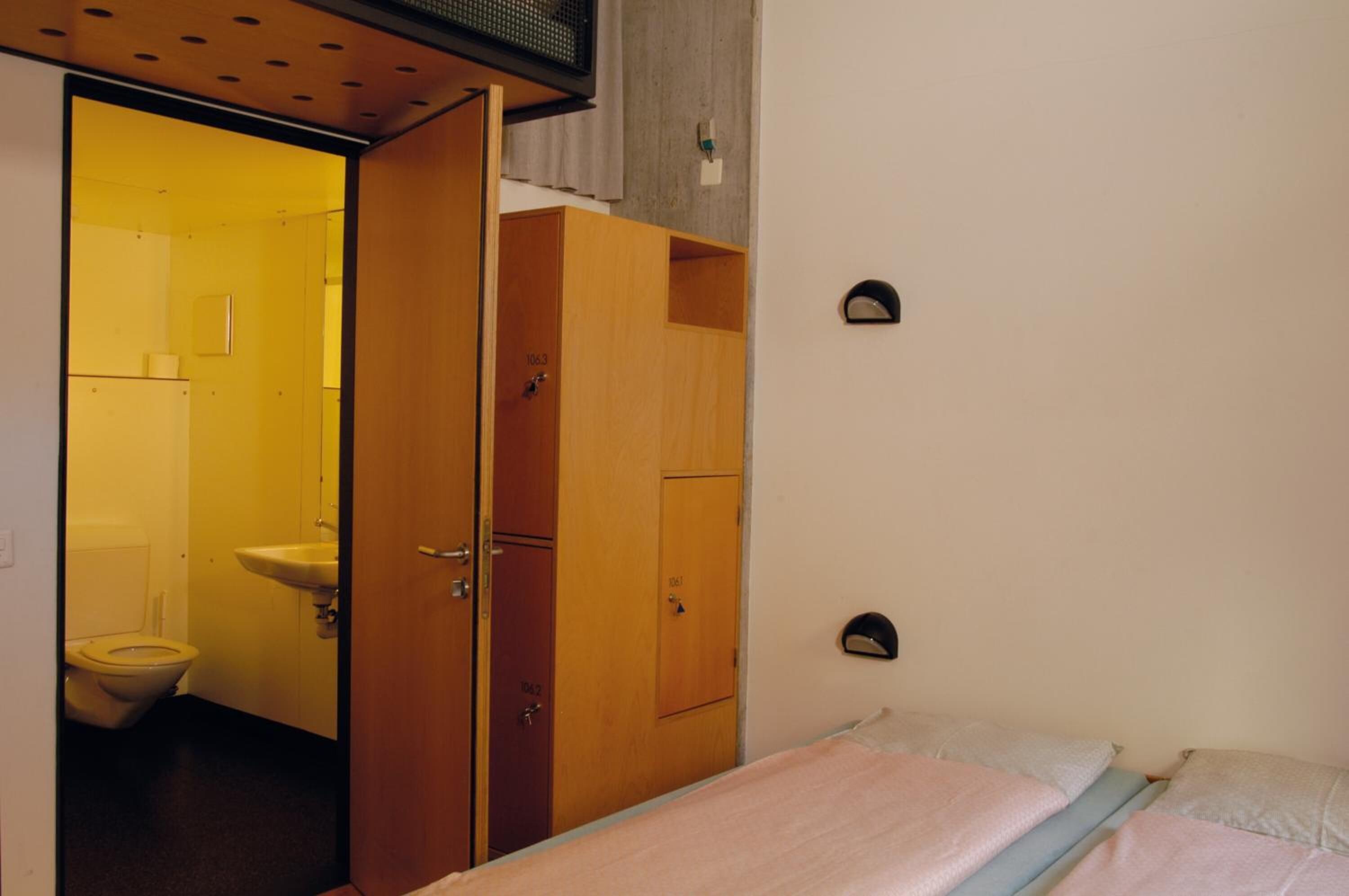 A compact room with a bed, a wooden wardrobe, and a bathroom visible through an open door.