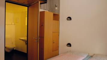 A compact room with a bed, a wooden wardrobe, and a bathroom visible through an open door.