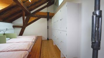 A room with wooden beams, a bed with pink bedding, and white lockers along the wall.
