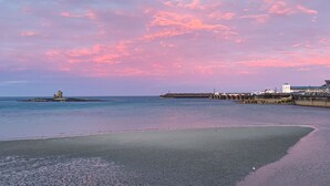 A beach with a calm sea, a distant pier, and a small island with a tower. - Cunard Apartments (Douglas)