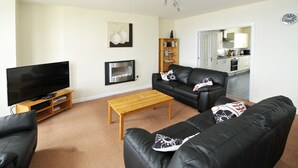 A living room with a flat-screen TV, a wooden coffee table, and black leather sofas. - Cunard Apartments (Douglas)