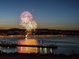 Un paisaje urbano frente al agua con un espectáculo de fuegos artificiales sobre el mar.