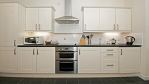 A kitchen with white cabinets, a stainless steel range hood, a microwave, and a double oven. - Cunard Apartments (Douglas)