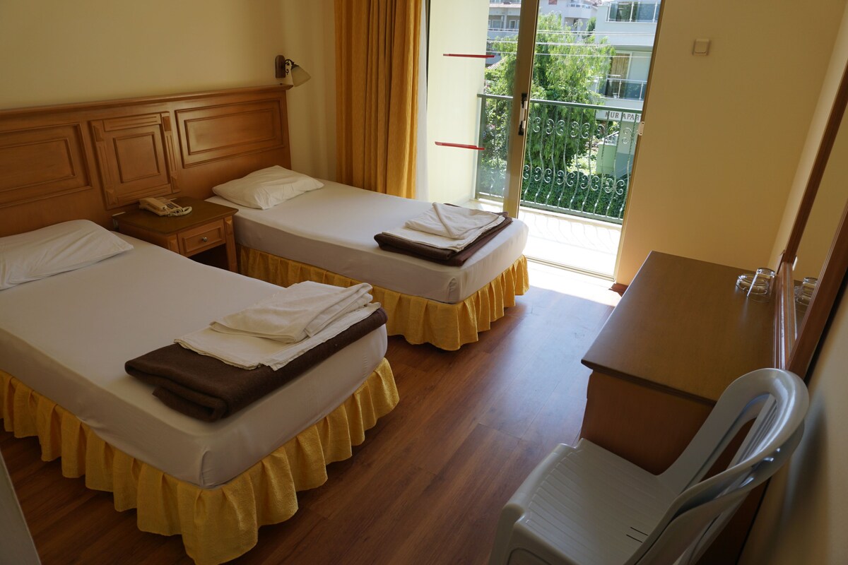 A hotel room with two beds, a desk, a chair, and a balcony with a view.