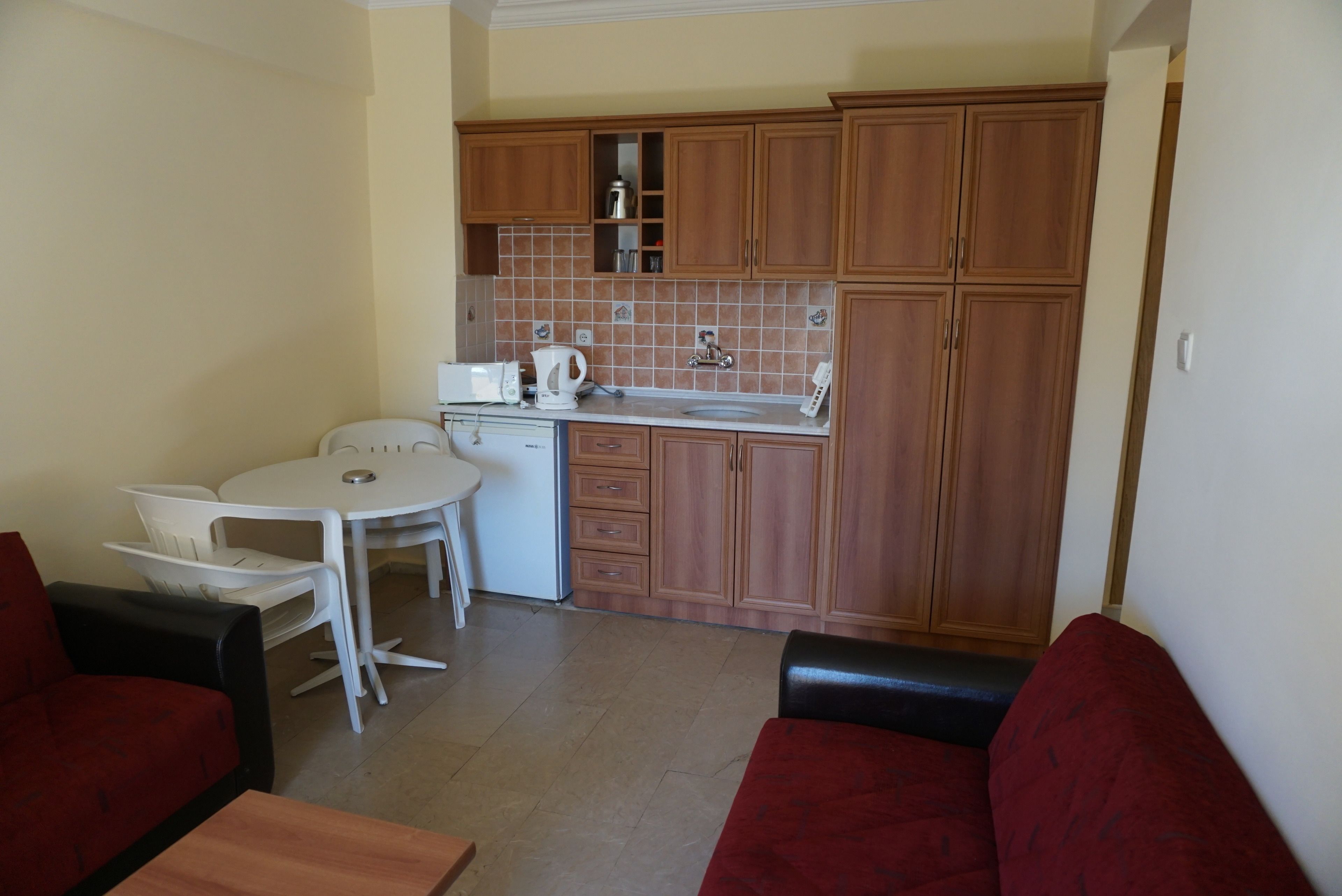 Een knus woongedeelte met een kitchenette, een eethoek met een tafeltje en stoelen, en een zithoek met een bank en een fauteuil.