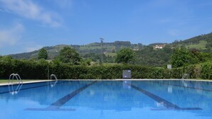 A rectangular swimming pool with clear blue water, surrounded by lush greenery and hills in the background. - El Solar del Mazo (Voto)