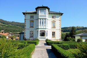 Un edificio grande y histórico con una torre central, rodeado de jardines bien cuidados y vistas despejadas del campo.