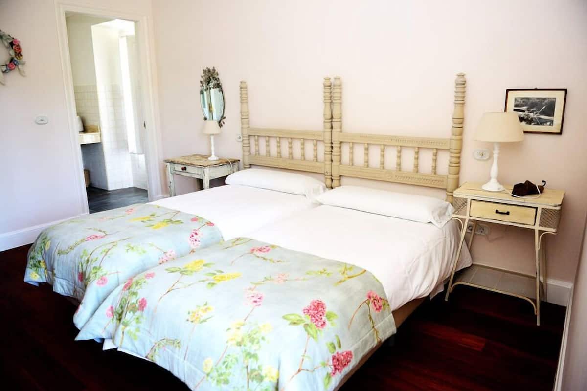 A double bed with floral bedding, a bedside table with a lamp, and a small cabinet.