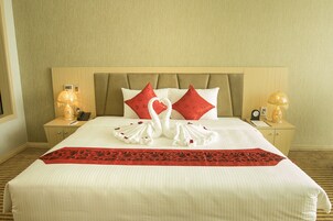 A neatly made bed with a red and white pillow arrangement, a red and black bed runner, and two bedside lamps on wooden nightstands.