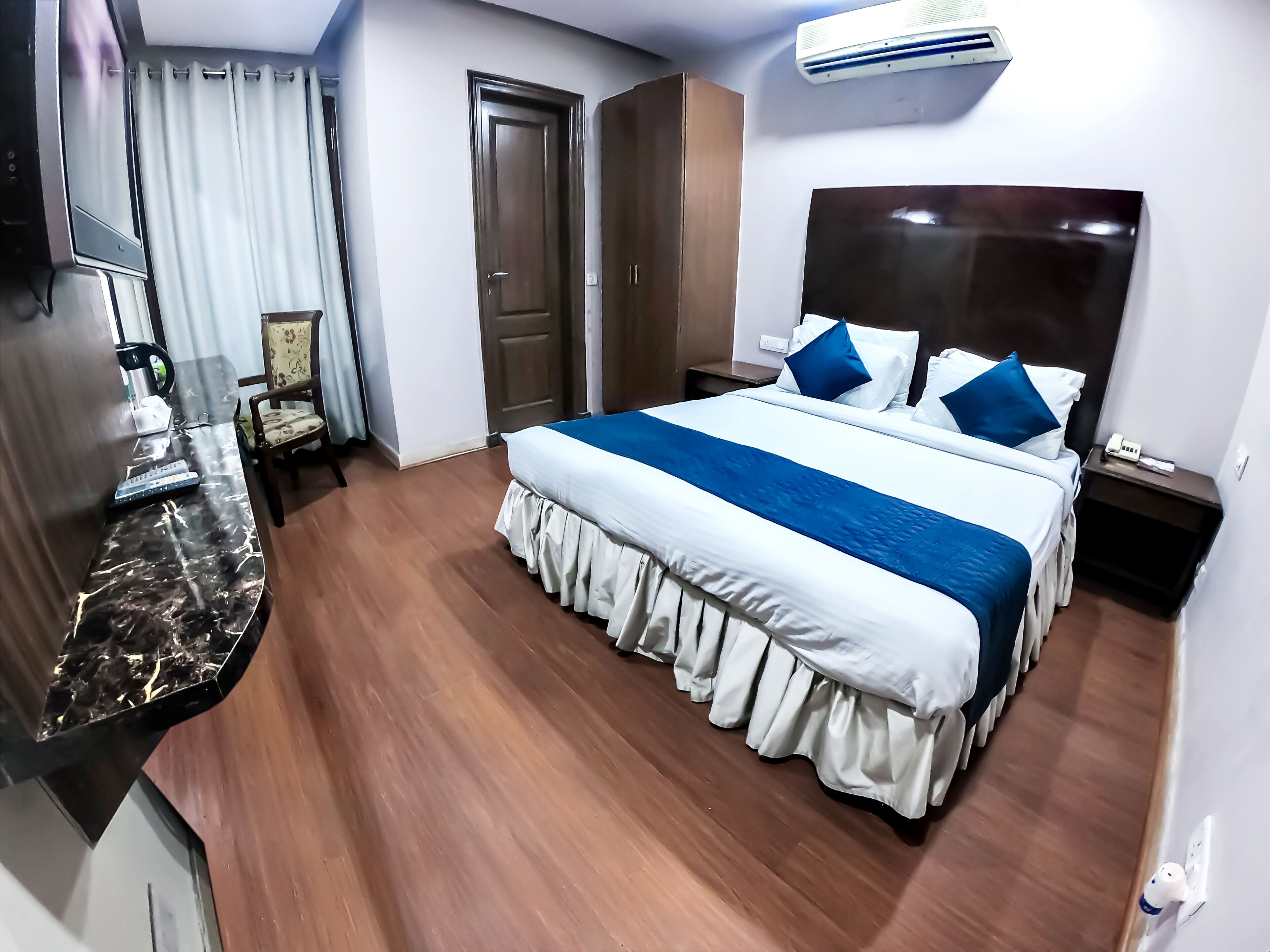A hotel room with a bed, a desk, a chair, a coffee maker, and an air conditioner.