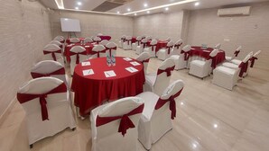 A conference room with round tables, white chairs with red sashes, and a whiteboard on the wall. - Kastor International (New Delhi)