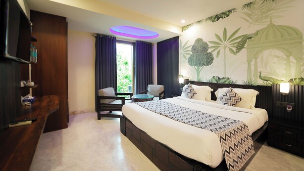 A hotel room with a large bed, a desk, a chair, and a view of the outdoors. - Kastor International (New Delhi)