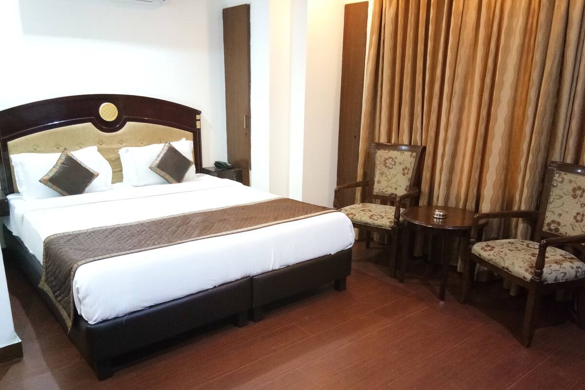 A hotel room with a large bed, two chairs, a small table, and a mirror.
