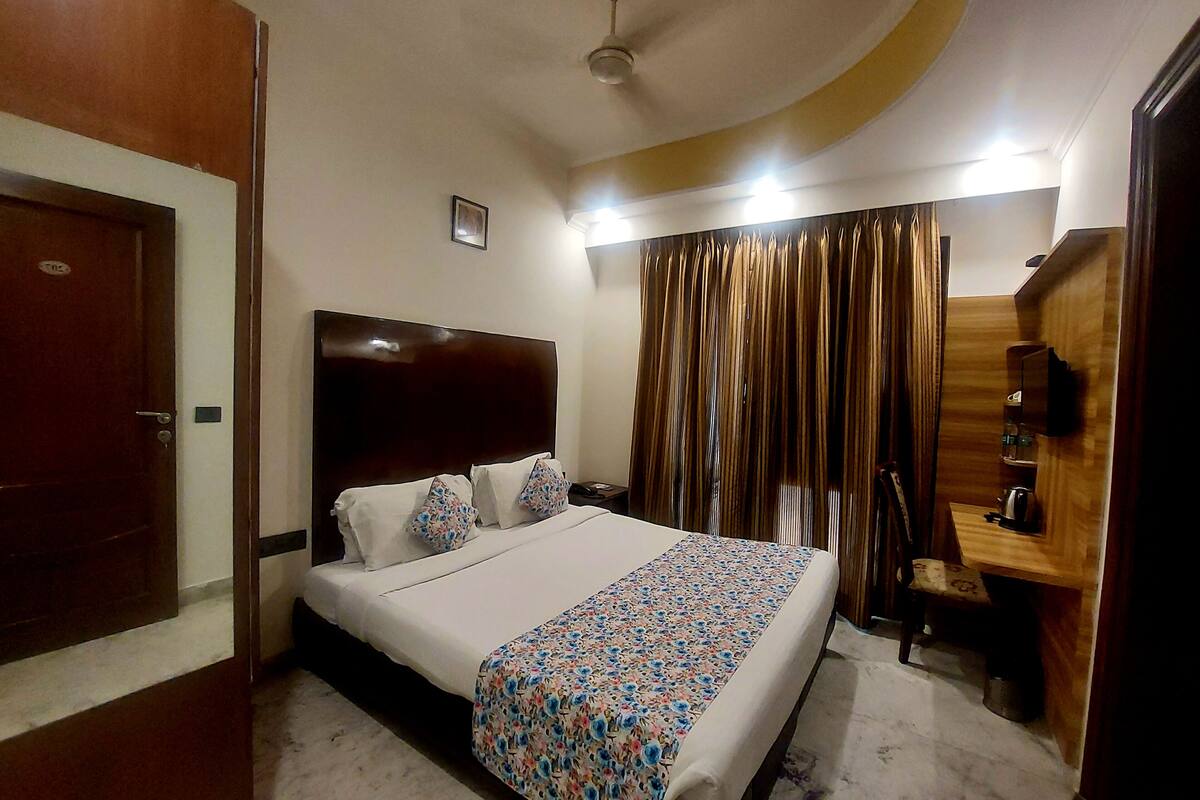 A bedroom with a large bed, a wooden headboard, a bedside table with a lamp, a wardrobe, and a curtain.
