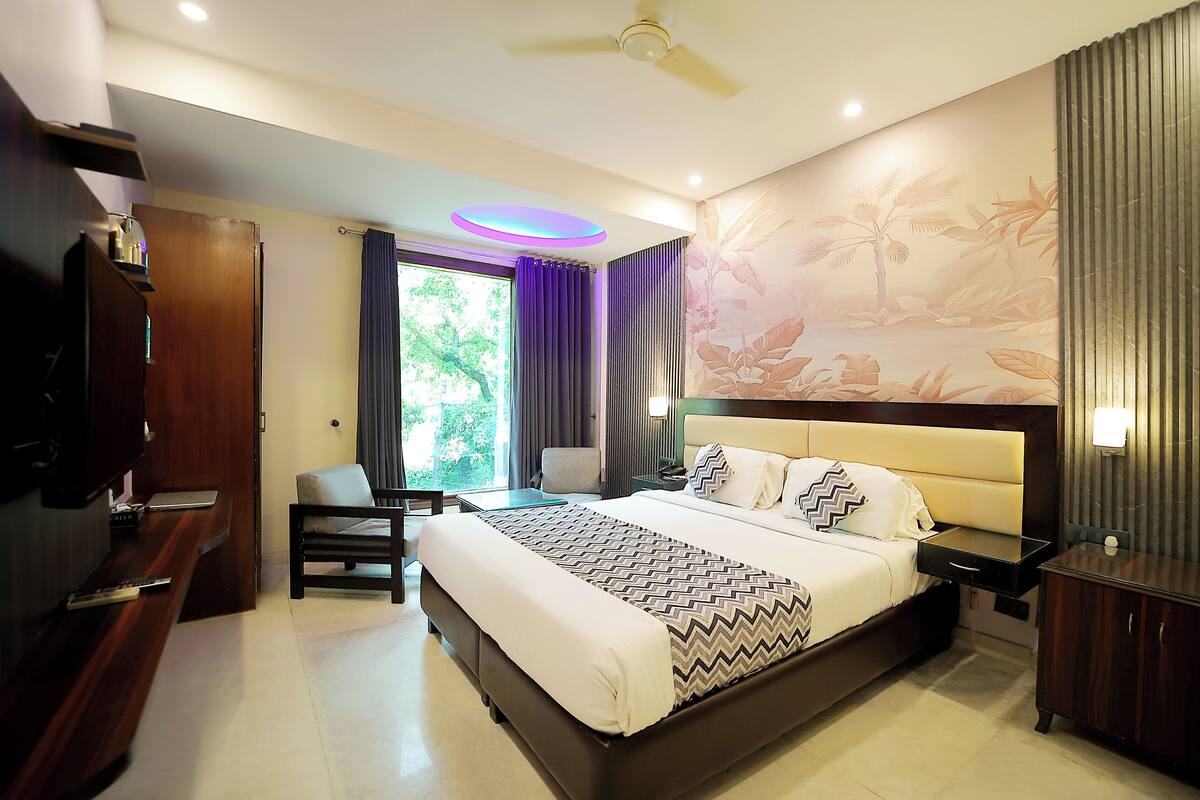 A hotel room with a large bed, a desk, a chair, a wardrobe, and a ceiling fan.