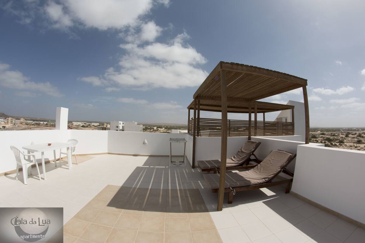 Eine Dachterrasse mit Holz-Pergola, Liegestühlen, einem Tisch und Stühlen.