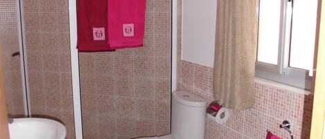 Un baño con ducha, dos inodoros, un lavamanos y un espejo.