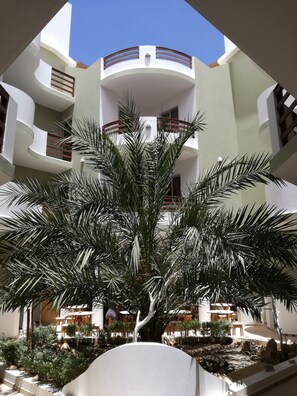 A multi-level building with balconies, a central palm tree, and outdoor seating areas. - Cala Da Lua (Boa Vista)
