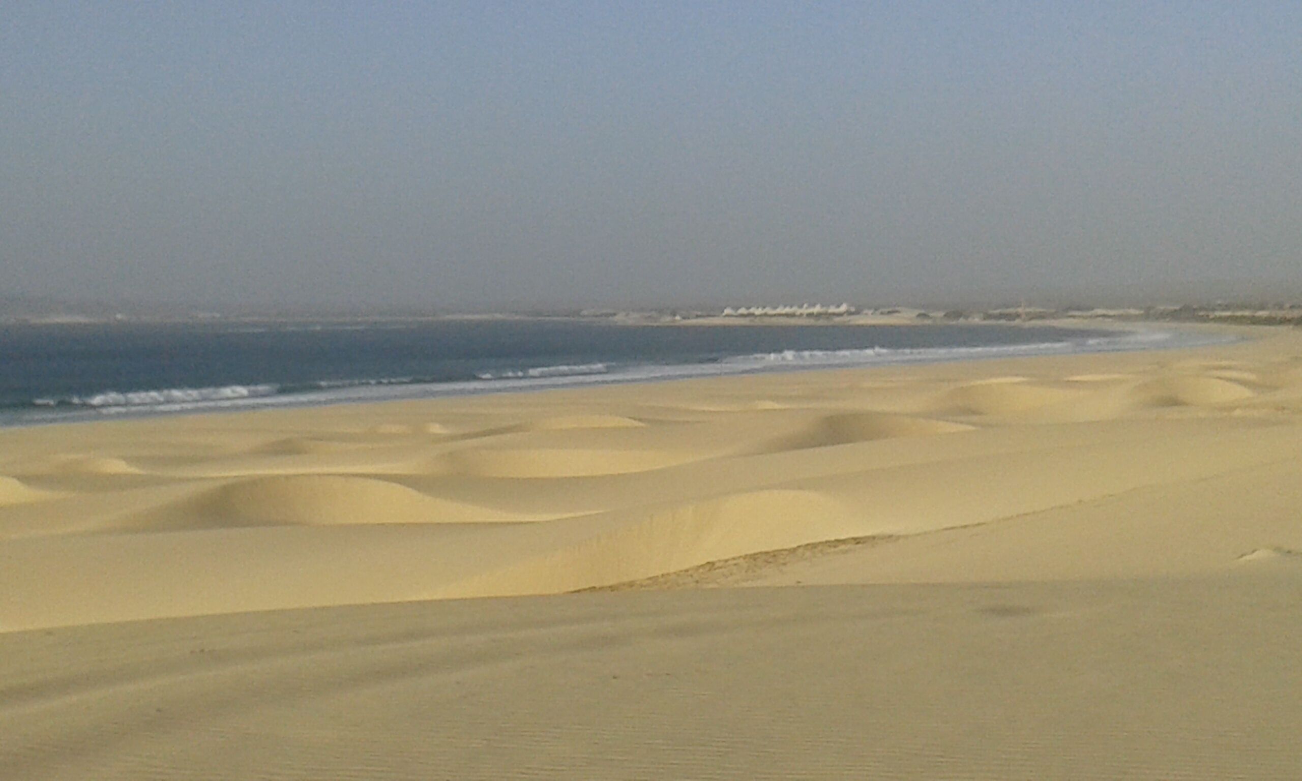 Une plage avec des dunes de sable et l’océan en arrière-plan.