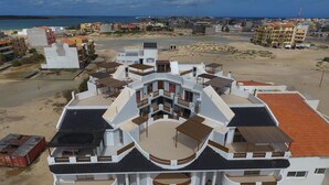 A multi-story hotel with balconies, a beach view, and a coastal cityscape in the background. - Cala Da Lua (Boa Vista)