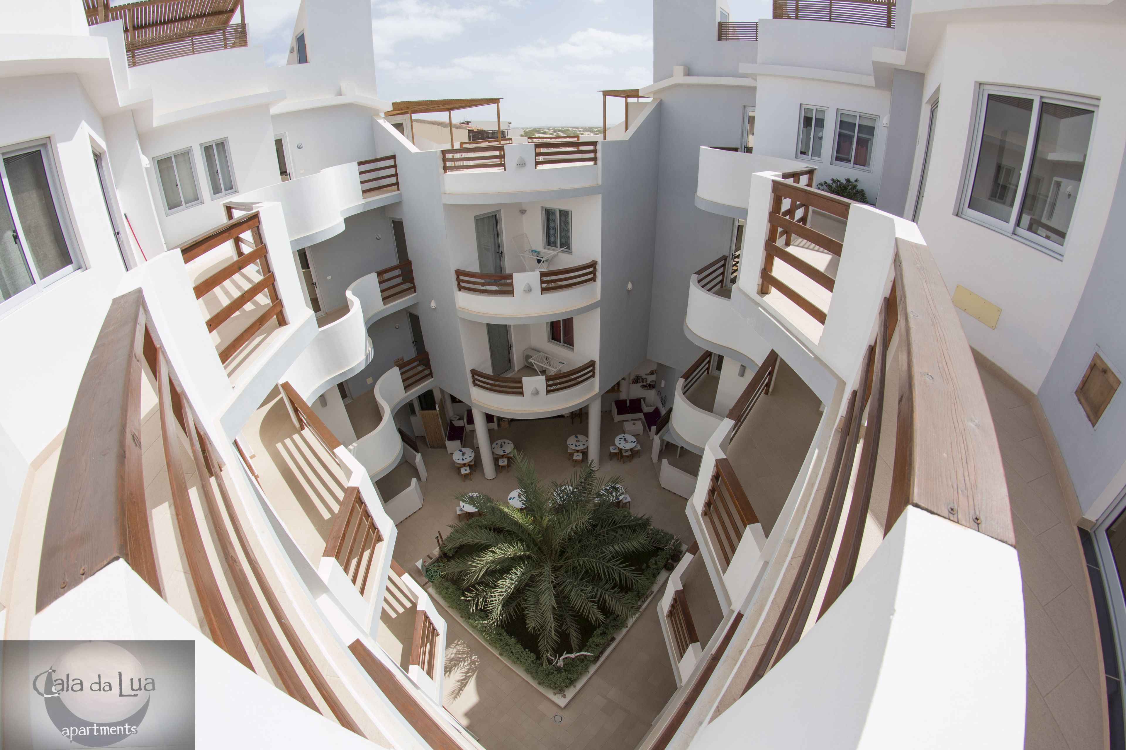 A multi-level residential building with balconies, a central courtyard with a palm tree, and outdoor seating areas.