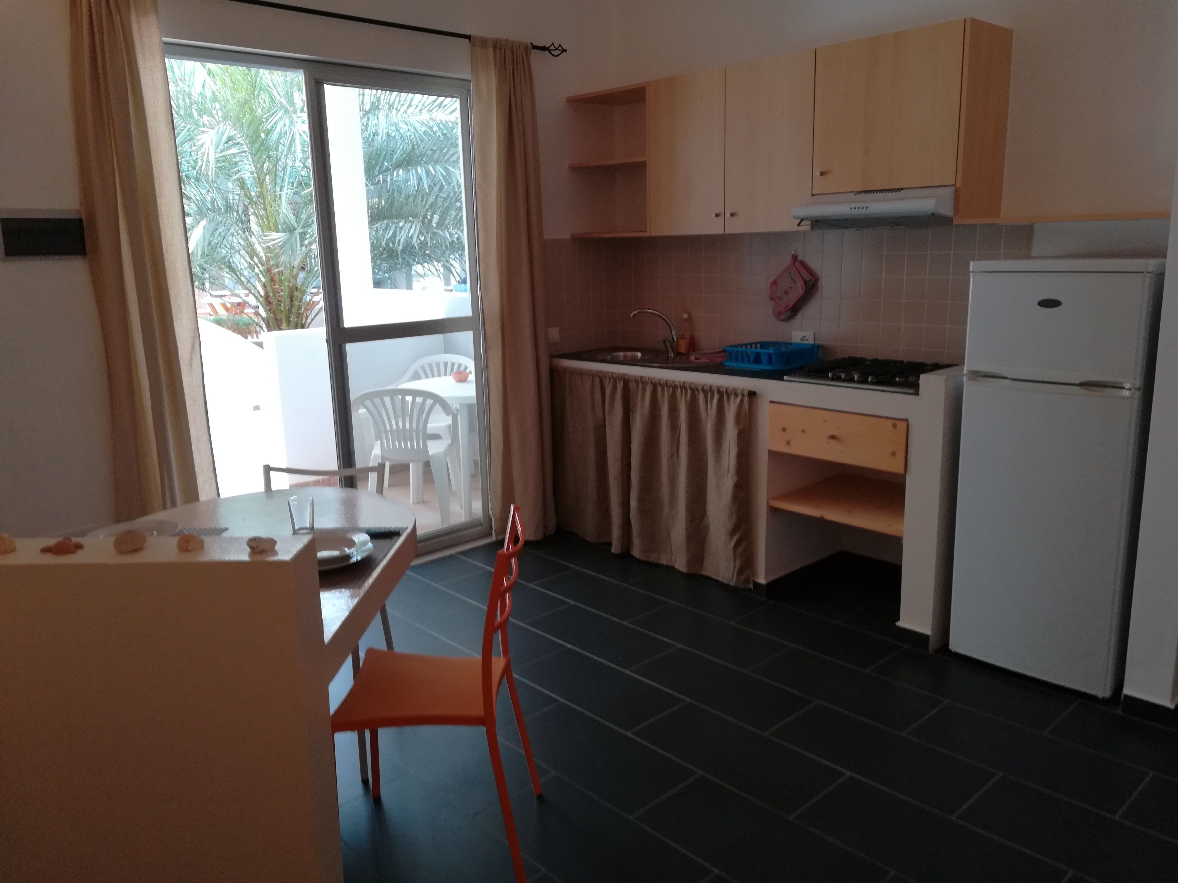 A compact kitchen with a dining area, a refrigerator, a stove, and a window with curtains.