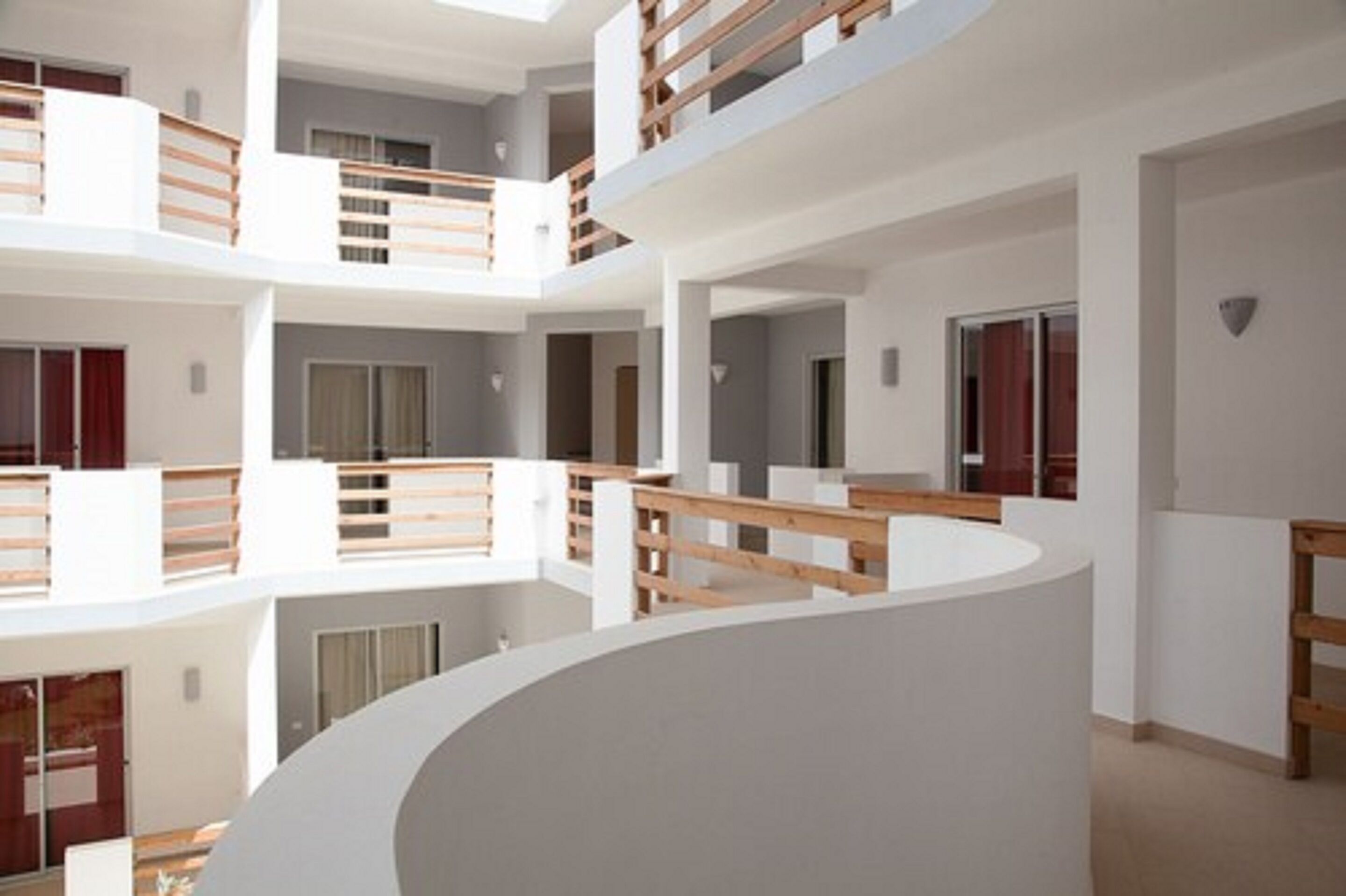 Un interior de varios niveles con balcones, paredes blancas y barandas de madera.