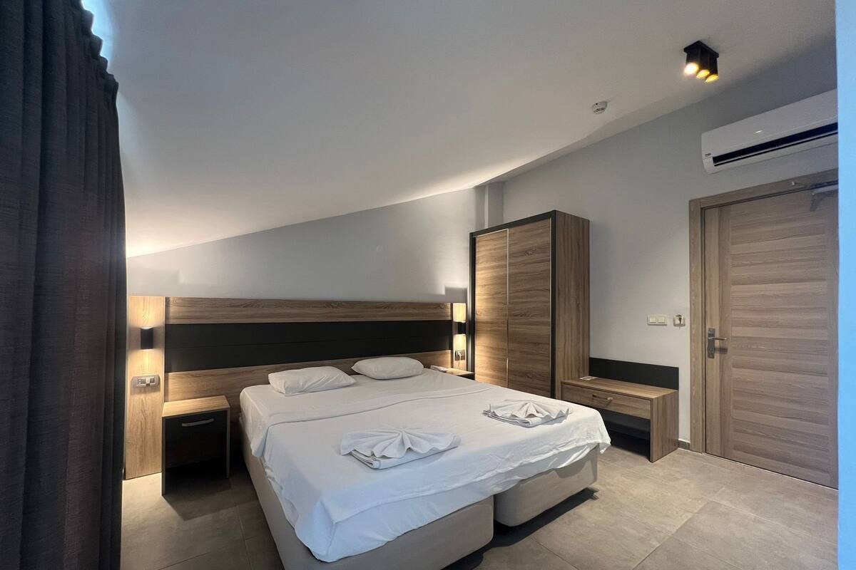 Une chambre d’hôtel moderne équipée d’un grand lit, de tables de chevet, d’une armoire et d’un appareil de climatisation.