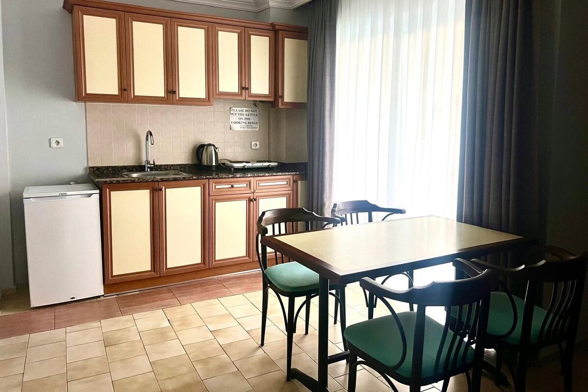 A compact kitchen with wooden cabinets, a white refrigerator, a sink, and a dining table with chairs.