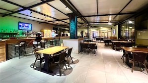 Een ruim restaurant met veel eettafels en stoelen, een bar met een televisiescherm, en diverse zitmogelijkheden.