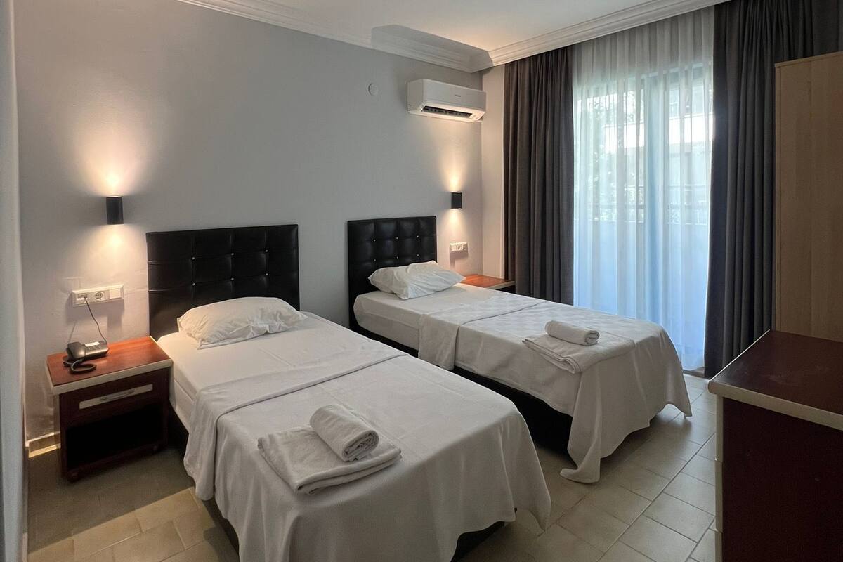 Une chambre d’hôtel avec deux lits, une table de chevet avec une lampe, un appareil de climatisation et une armoire.