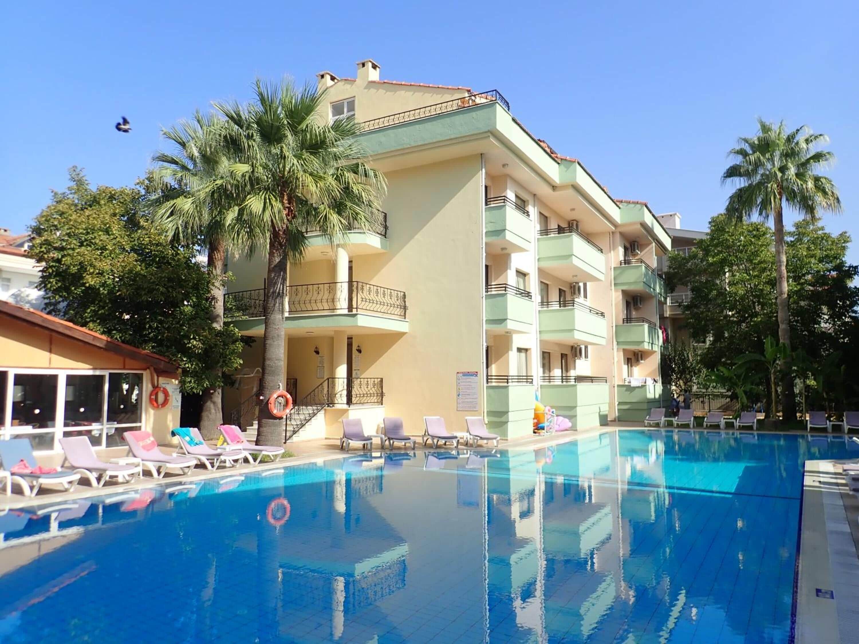 A hotel with a swimming pool, multiple balconies, and palm trees.